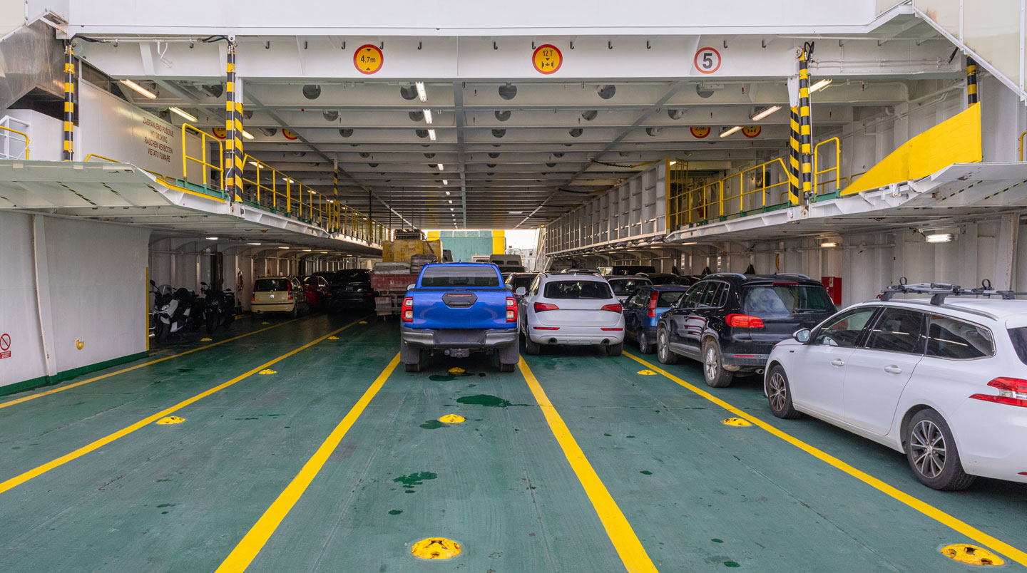 File de véhicules ordonnée dans la zone de pré-embarquement d'un port méditerranéen, agents en gilet fluorescent orientant les conducteurs